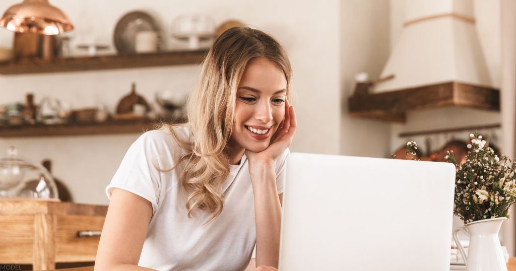 Blond woman smiling and working on laptop. (MODEL)